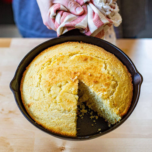 Handcrafted pre-seasoned cast iron skillet holding a freshly baked golden cornbread with a wedge removed, highlighting exceptional heat retention for Kitchen & Food, Cookware, Cast Iron, Best Sellers, Promo Eligible collections.