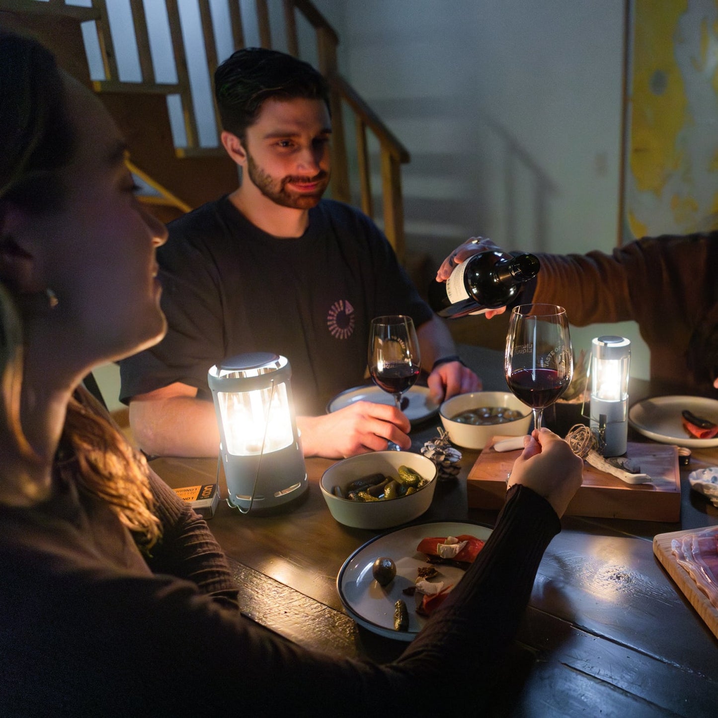 Two handcrafted Candlelier Candle Lanterns with bright warm light illuminate an intimate indoor dinner scene, featuring wine glasses and rustic tableware, perfect for cozy gatherings.