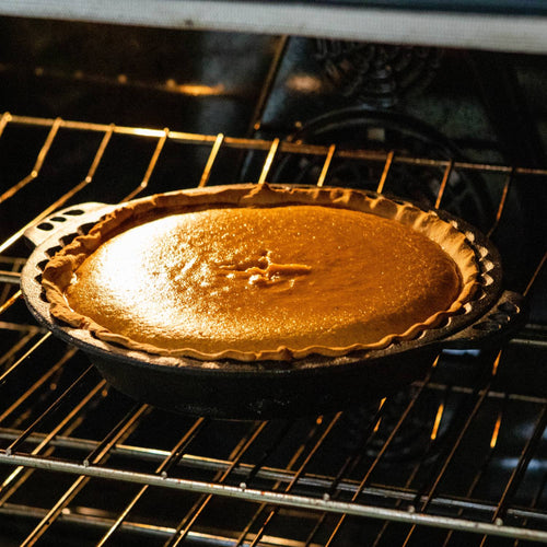 Handcrafted cast iron pie pan with decorative crimped edges baking a golden brown pie, featured in Kitchen & Food, Cookware, Cast Iron, Baking Supplies, and Best Sellers collections.