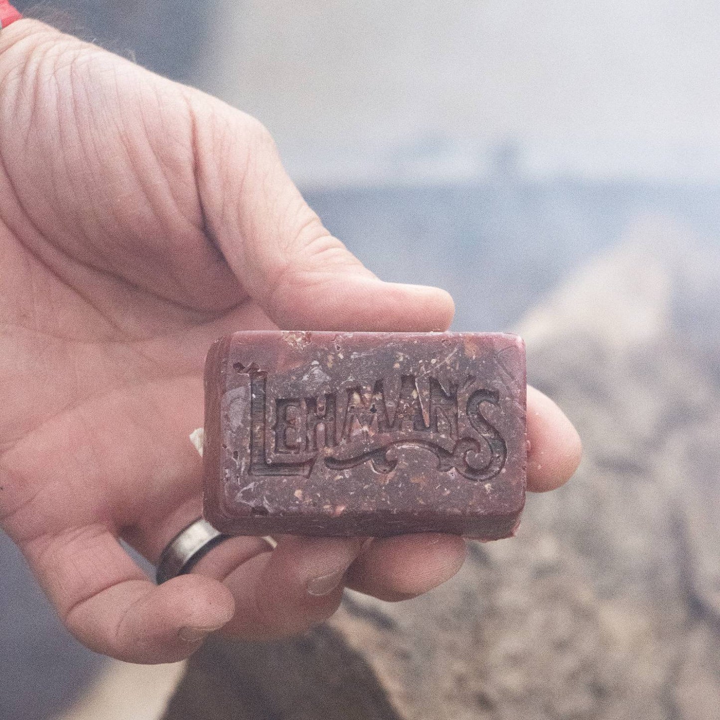 Handcrafted reddish-brown fire starter block with embossed Lehman's logo, made in USA from natural reclaimed wax and sawdust, shown held for Farm, Garden & Tool, Camping, and Hearth Accessories collections.