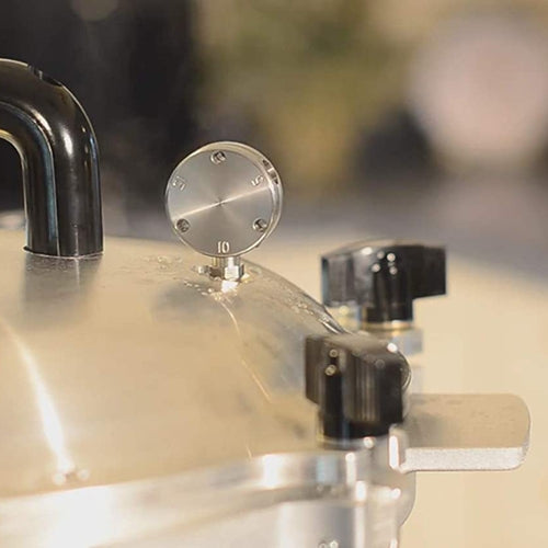 Close-up view of a stainless steel pressure gauge and black control knobs on a 30-quart pressure canner, handcrafted in USA, ideal for food preservation and homesteading collections.