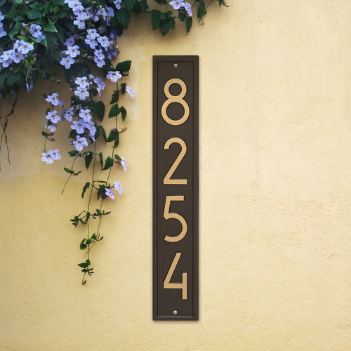 Handcrafted vertical aged bronze address plaque with clean modern numerals mounted on a light yellow wall near purple flowering vines, enhancing curb appeal in Home & Decor, Household Helpers, Mailboxes and Address Signs, USA Made, and Best Sellers collections.