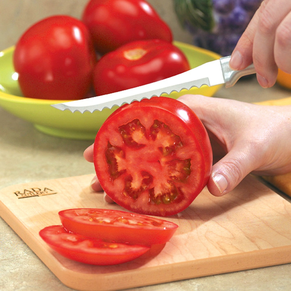 Handcrafted Rada tomato slicer with hand-sharpened high carbon surgical stainless steel serrated blade and solid aluminum handle slicing fresh tomato on wooden cutting board, USA Made collections.