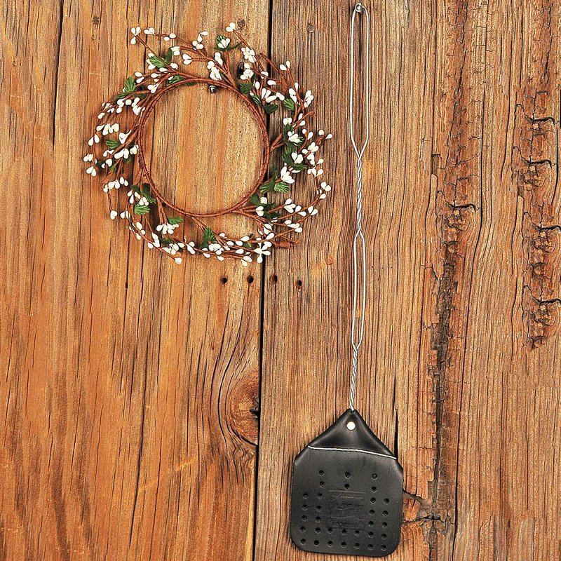 Hand-sewn leather fly swatter with a 15-inch wire handle, made in the USA by Amish craftsmen, displayed on rustic wood alongside a decorative grapevine wreath with white berries.