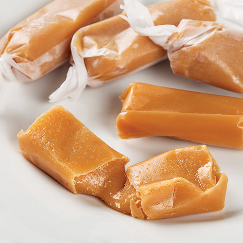 Soft, buttery caramel pieces hand wrapped in waxed paper, showcasing a homemade-style treat made in the USA, perfect for Kitchen & Food and Snacks and Sweets collections.