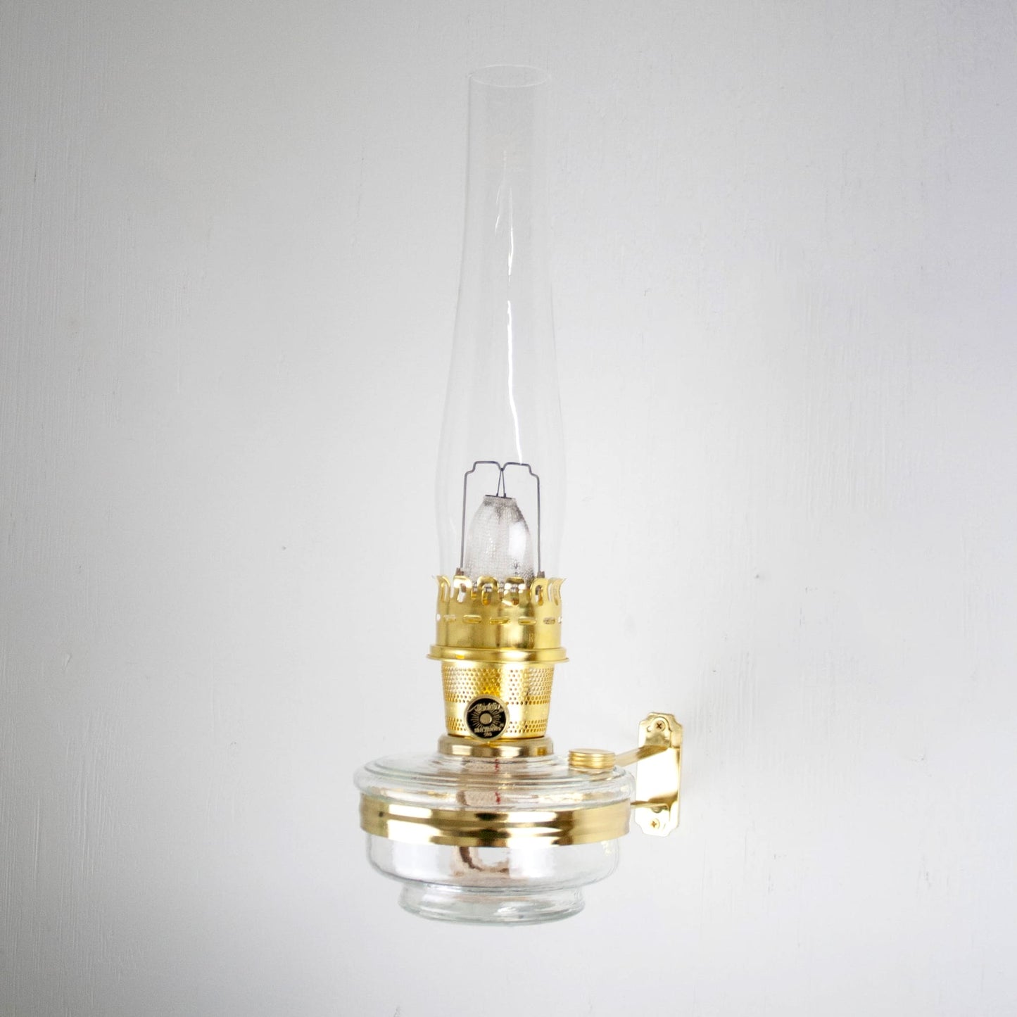 Handcrafted brass wall bracket with clear glass oil lamp and tall chimney, designed for classic Aladdin lamps, featured in Lamps & Lighting, Oil Lamps, Wall Lamps, Best Sellers, and Promo Eligible collections.