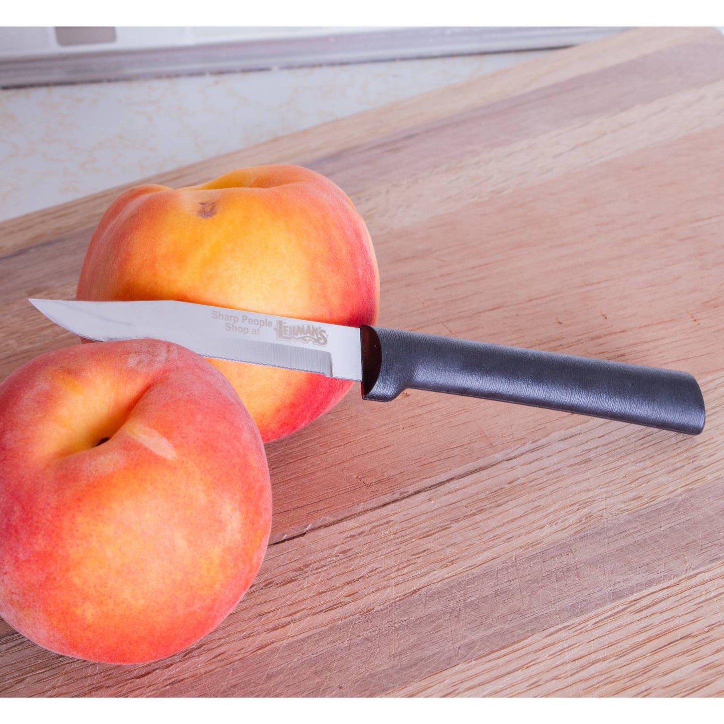 Handcrafted serrated paring knife with finely toothed blade and smooth black handle, made in USA, shown with fresh peaches on wooden cutting board, ideal for food prep and farm, garden & tool collections.