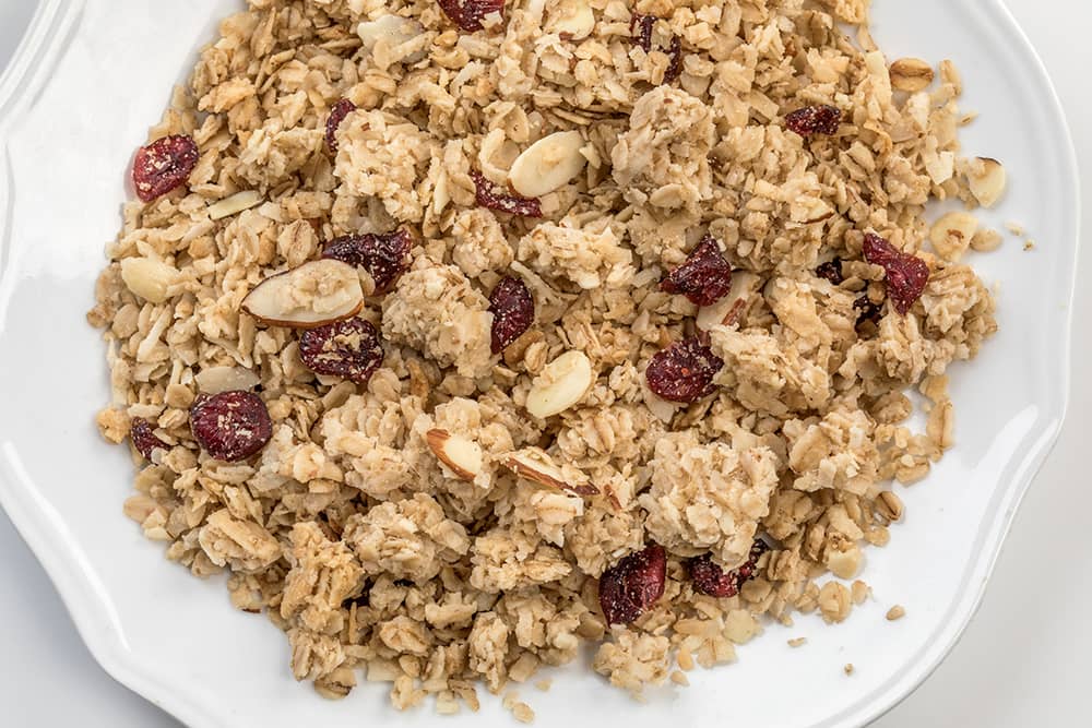 Close-up of handcrafted Amish-made granola clusters with whole grain oats, dried cranberries, and sliced almonds on a white plate, featured in Kitchen & Food and USA Made collections.