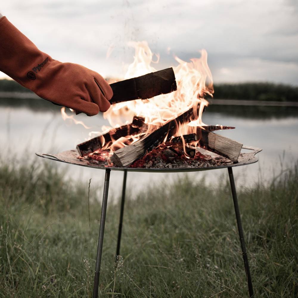 Outdoor steel fire bowl with three sturdy legs in a natural setting by a lake, ideal for camping, farm, garden, and tool use in popular best sellers and promo collections.