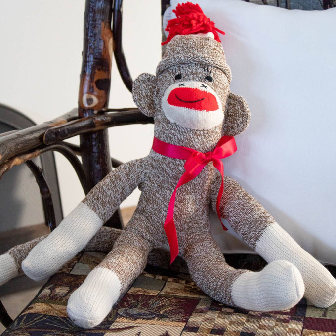 Hand-sewn sock monkey made in USA from classic red and white heel socks, featuring a bright red pom-pom hat and red ribbon bow, perfect for indoor play and children’s toys collections.