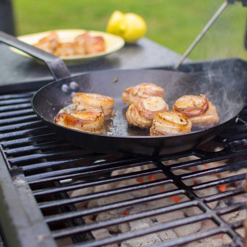 Seasoned steel skillet cooking seared meat medallions on an outdoor grill, showcasing durable cookware designed for Kitchen & Food, Cookware, Pots and Pans, USA Made, Best Sellers, and Promo Eligible collections.