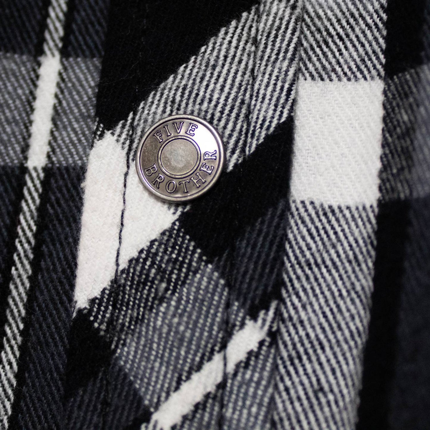 Close-up of a handcrafted black and white plaid flannel fabric with detailed woven texture and a branded metal snap button, featured in clothing and health collections.