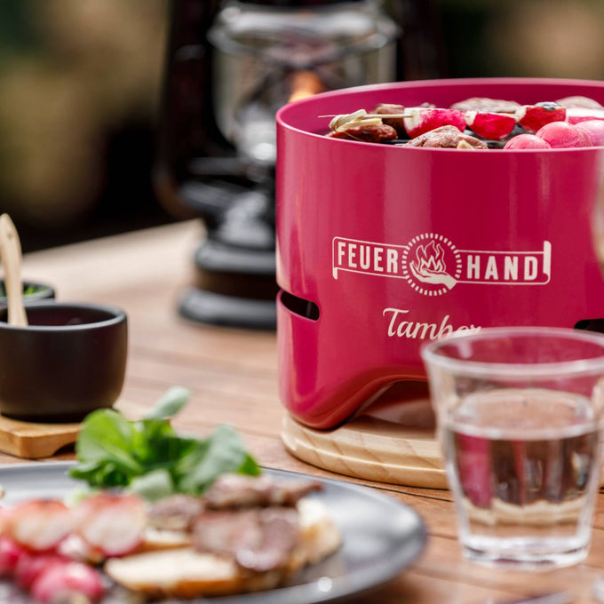 Handcrafted pink tabletop charcoal grill with skewers cooking over low heat, set on a wooden table with glassware and outdoor dining accents, perfect for Farm, Garden & Tool, Camping, and Grilling collections.