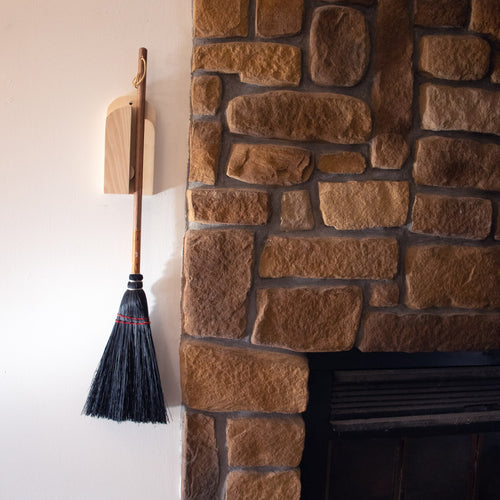 Handcrafted Amish made wooden wall-mounted broom holder securely storing a traditional broom next to a rustic stone fireplace, featured in Home & Decor and Household Helpers collections.