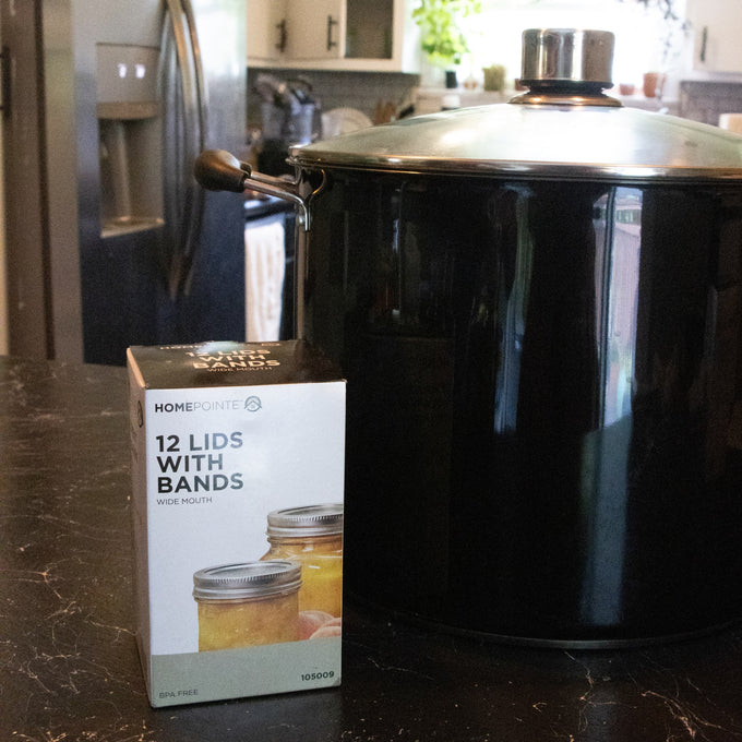 Box of 12 wide-mouth canning jar lids with metal bands featuring BPA-free sealing compound, displayed next to a large black stockpot on a kitchen countertop, ideal for Kitchen & Food, Food Preservation, and Canning collections.