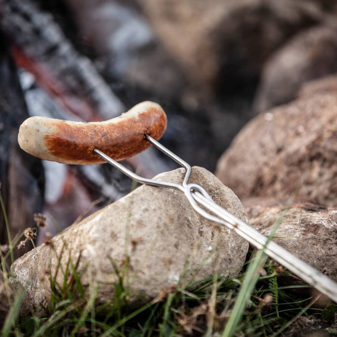 Handcrafted metal skewer with adjustable handle roasting a sausage safely over campfire flames, perfect for Farm, Garden & Tool, Camping, Best Sellers, and Promo Eligible collections.