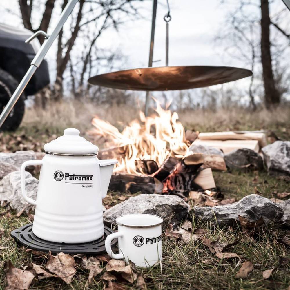 White enameled steel percolator and matching mug set placed on a cast iron trivet near a campfire with hanging cooking plate, ideal for camping and outdoor brewing, featured in Farm, Garden & Tool, Kitchen & Food, Camping, Brewing Coffee and Tea, Best Sellers, and Promo Eligible collections.