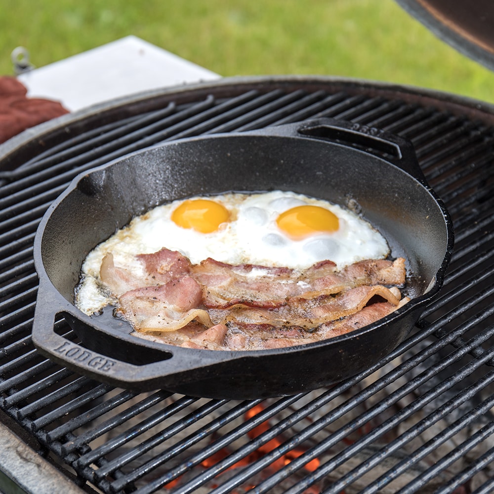 Handcrafted cast iron round pan with short side handles cooking two sunny-side-up eggs and crispy bacon on an outdoor grill, part of Kitchen & Food, Cookware, Cast Iron, Best Sellers, Promo Eligible collections.