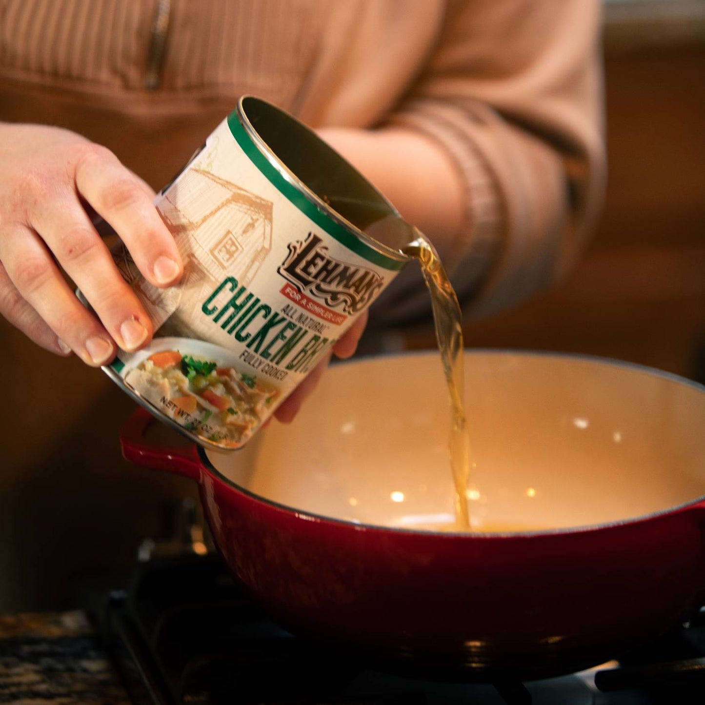 Person pouring Lehman's canned chicken broth into a red cooking pot on a stovetop, showcasing convenience for preparing soups and stews, part of Farm, Garden & Tool and Kitchen & Food collections.