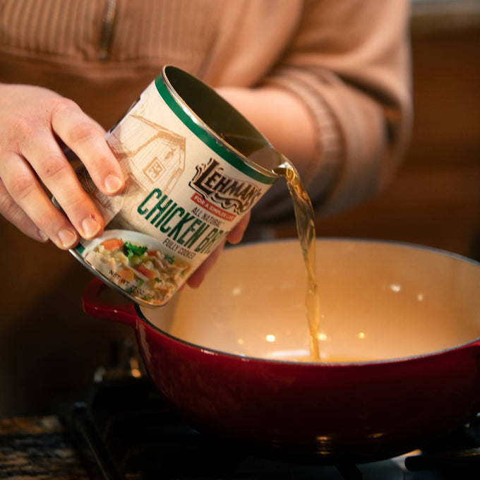 Person pouring Lehman's canned chicken broth into a red cooking pot on a stovetop, showcasing convenience for preparing soups and stews, part of Farm, Garden & Tool and Kitchen & Food collections.