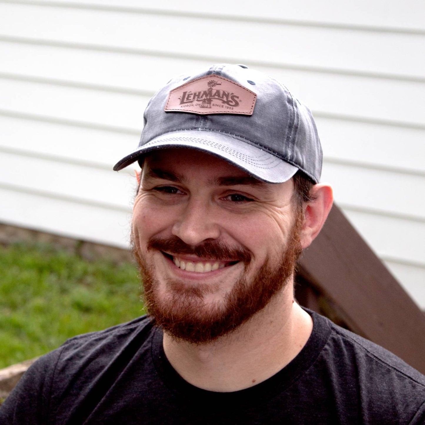 Smiling man wearing an adjustable retro-style cap with a vintage washed cotton look and a light brown leather patch featuring a windmill design, perfect for Health & Wellness and Clothing and Accessories collections.
