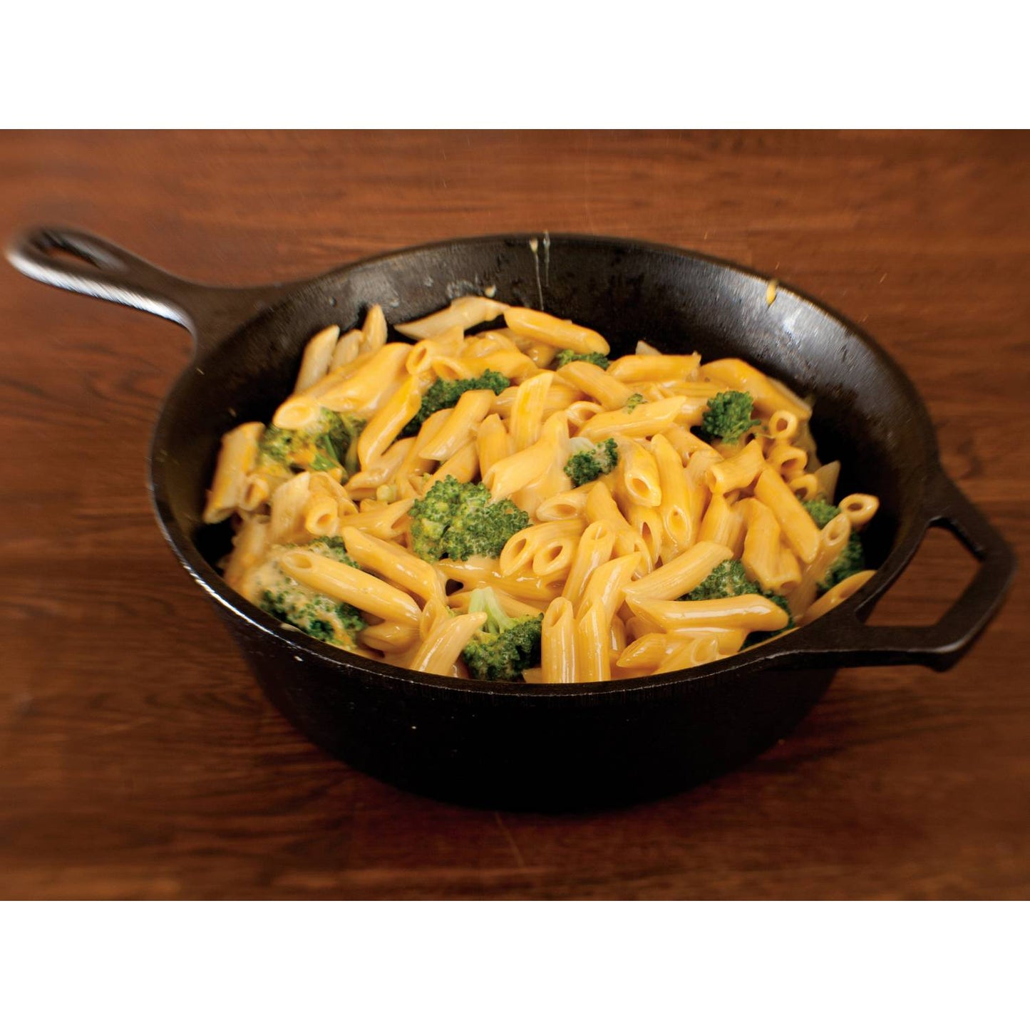 Black cast iron deep skillet filled with creamy macaroni and cheese mixed with broccoli, shown on a wooden surface, ideal for kitchen, camping, and cookware collections.