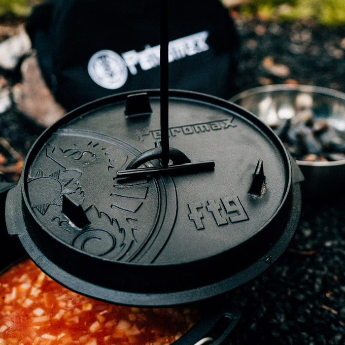 Close-up of a sturdy cast iron lid with embossed design and handle tool lifting it from a pot simmering richly colored stew, perfect for Kitchen & Food, Cookware, Cast Iron, Best Sellers collections.