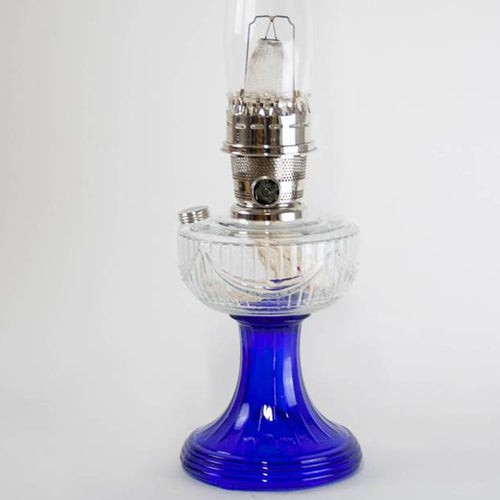 Handcrafted oil lamp with a clear glass font and vibrant cobalt blue base, featuring a nickel burner, perfect for Lamps & Lighting, Oil Lamps, Table Lamps, Best Sellers, and Promo Eligible collections.