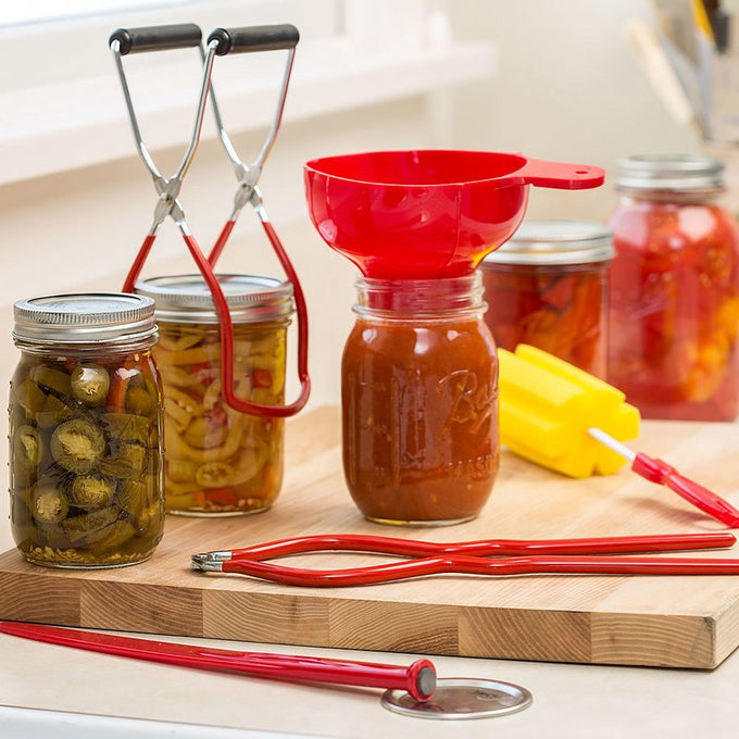 Set of handcrafted red and yellow canning tools including funnel, jar lifters, and magnetic lid wand, displayed with glass jars of preserved food for Kitchen & Food, Food Preservation, and Best Sellers collections.