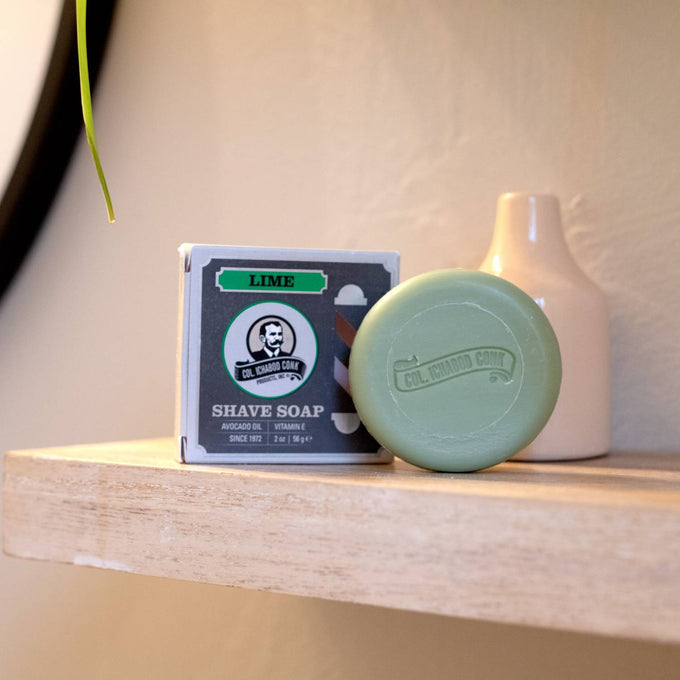 Handcrafted lime shaving soap puck embossed with brand logo, displayed next to its boxed packaging on a wooden shelf, featured in Health & Wellness, Grooming and Personal Hygiene, Soaps and Soapmaking, USA Made, Best Sellers, Promo Eligible collections.