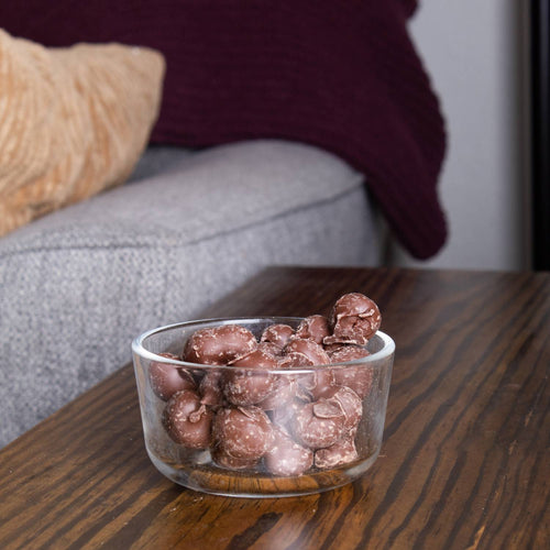 Clear glass bowl filled with handcrafted double-dipped chocolate peanuts on a wooden table, highlighting a unique treat from USA made Snacks and Sweets collections.