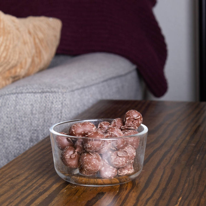 Clear glass bowl filled with handcrafted double-dipped chocolate peanuts on a wooden table, highlighting a unique treat from USA made Snacks and Sweets collections.