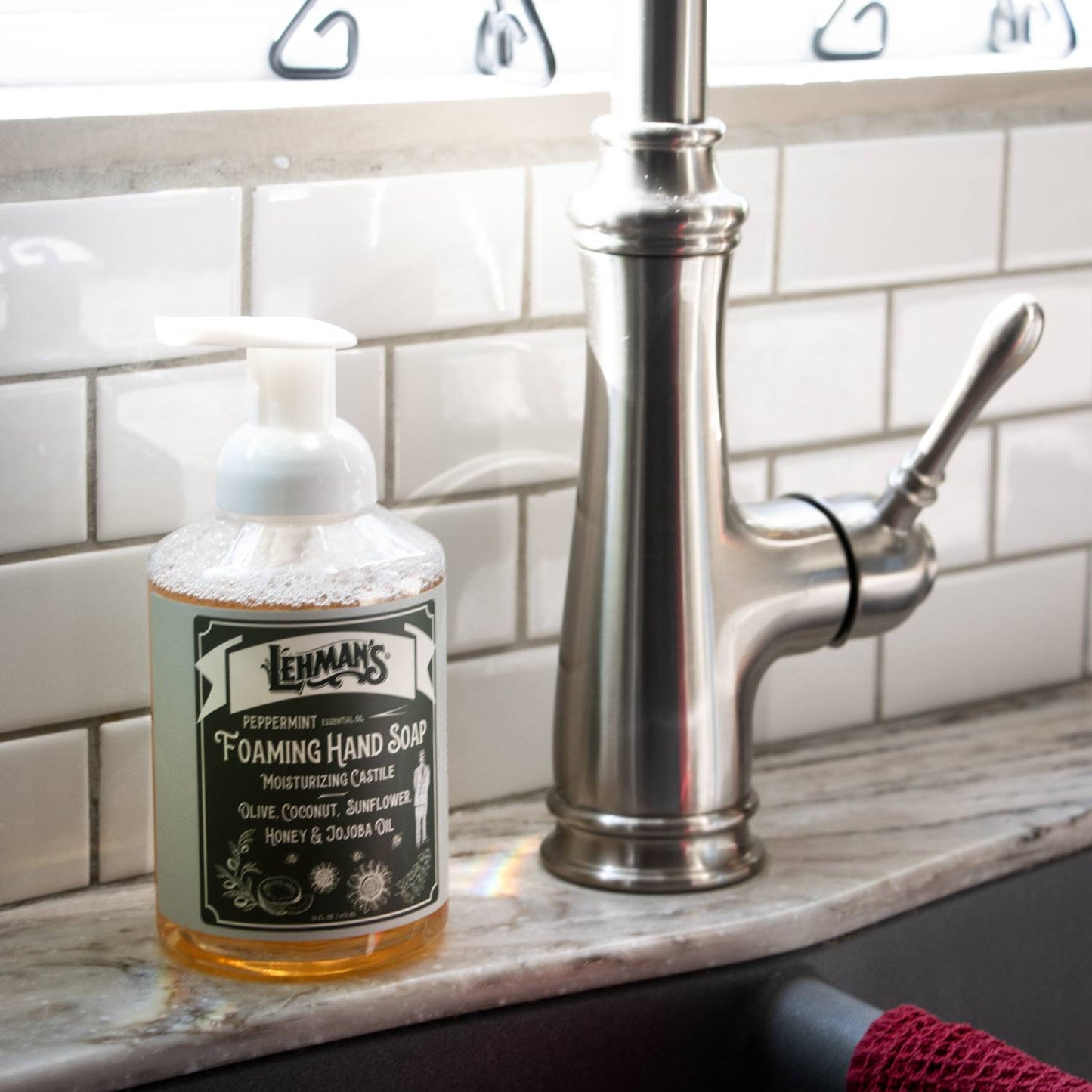 Clear pump bottle of Lehman's handcrafted moisturizing foaming hand soap with peppermint scent, made in USA using natural oils like olive, coconut, sunflower, honey, and jojoba, ideal for Health & Wellness, Grooming, and Soaps collections displayed beside a kitchen sink faucet.