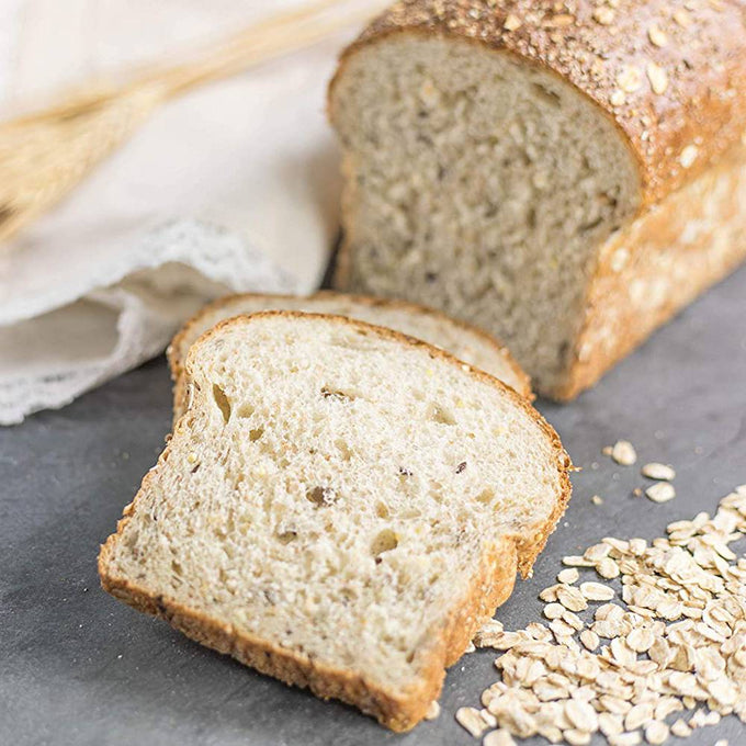 Close-up of two slices of homemade oat bread with a golden crust and seeds, alongside rolled oats, showcasing rustic baking in Kitchen & Food and Bread Making Supplies collections.