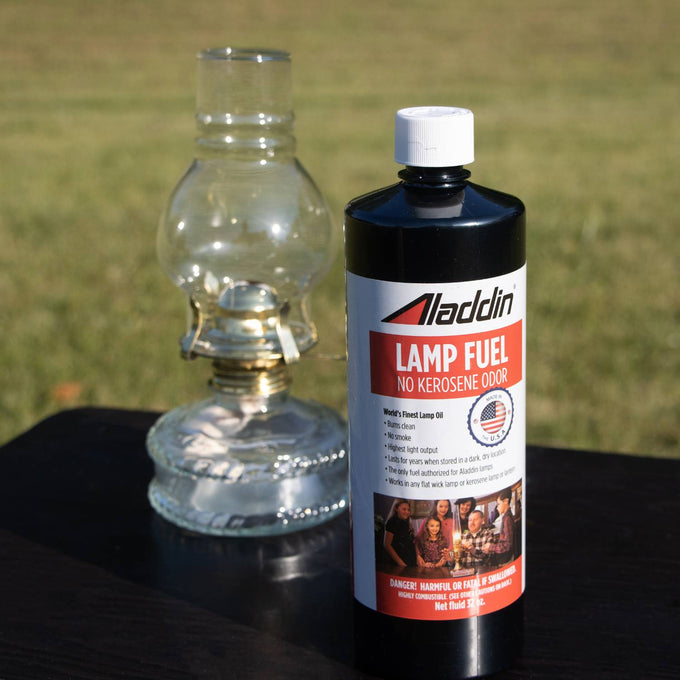 Black 32 oz bottle of clear lamp fuel labeled no kerosene odor standing outdoors beside a traditional glass oil lamp, suitable for Lamps & Lighting, Parts and Accessories, Lamp and Lantern Fuel, Best Sellers, and Promo Eligible collections.