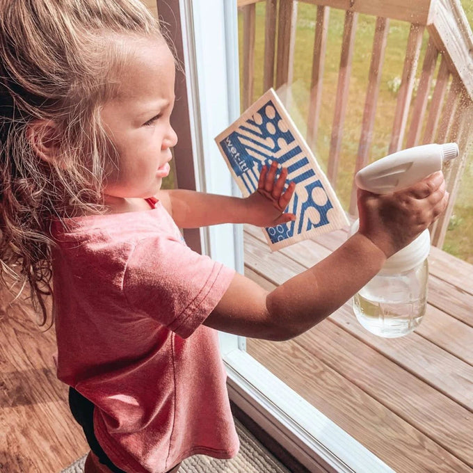 Young child holding a glass jar with a white sprayer lid while cleaning a window, highlighting eco-friendly home cleaning tools from Home & Decor, Household Helpers, USA Made collections.