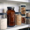 Collection of clear and amber glass jars with dark gray leak-resistant screw-on lids, filled with various pantry staples, displayed on a kitchen shelf for storage and serving in Kitchen & Food, Storage and Serving, Best Sellers, Promo Eligible collections.