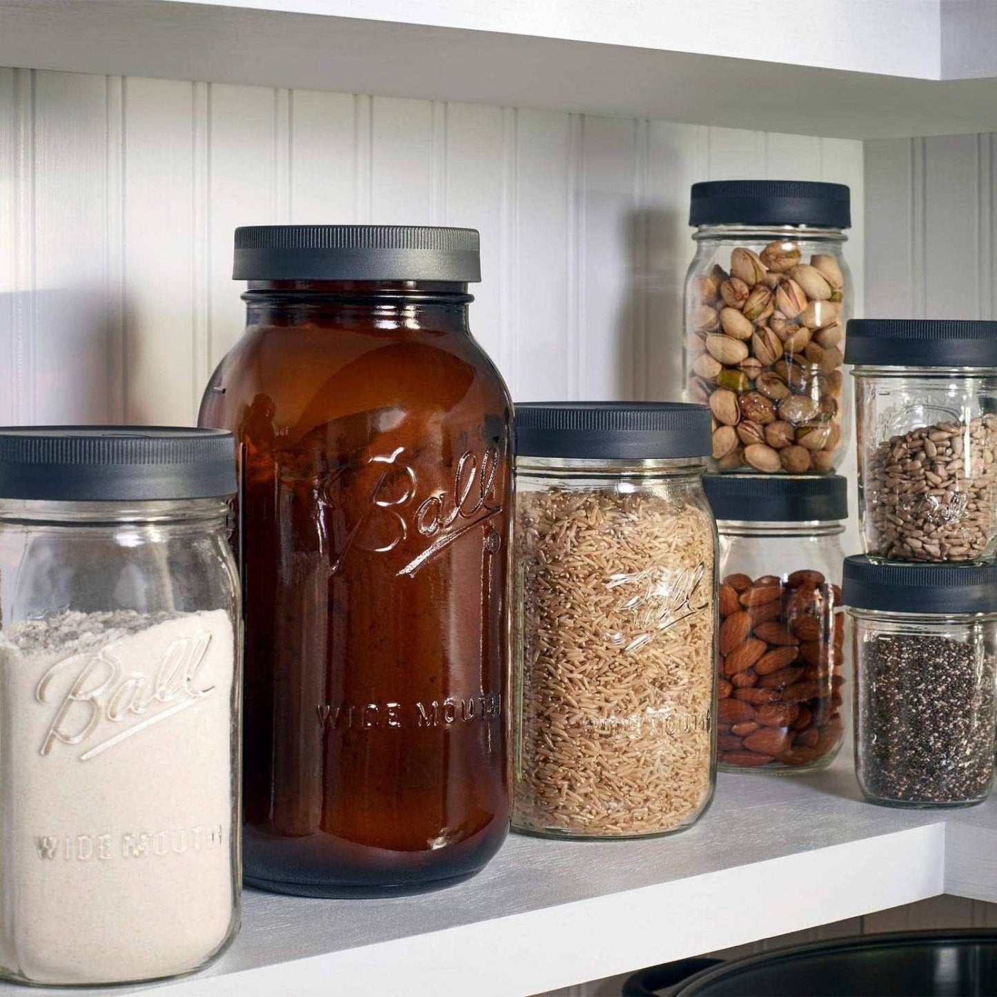 Collection of clear and amber glass jars with dark gray leak-resistant screw-on lids, filled with various pantry staples, displayed on a kitchen shelf for storage and serving in Kitchen & Food, Storage and Serving, Best Sellers, Promo Eligible collections.