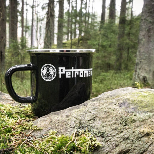 Black enameled steel camping mug with metal rim and bold logo, resting on mossy ground near a forest rock, ideal for Farm, Garden & Tool, Camping, and Brewing Coffee and Tea collections