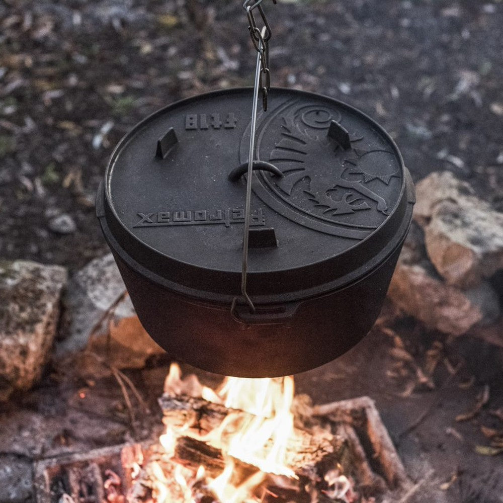 Seasoned cast iron pot with flat base featuring a cast lid embossed with a sun design, suspended over a campfire, ideal for Kitchen & Food, Cookware, Cast Iron, Best Sellers collections.