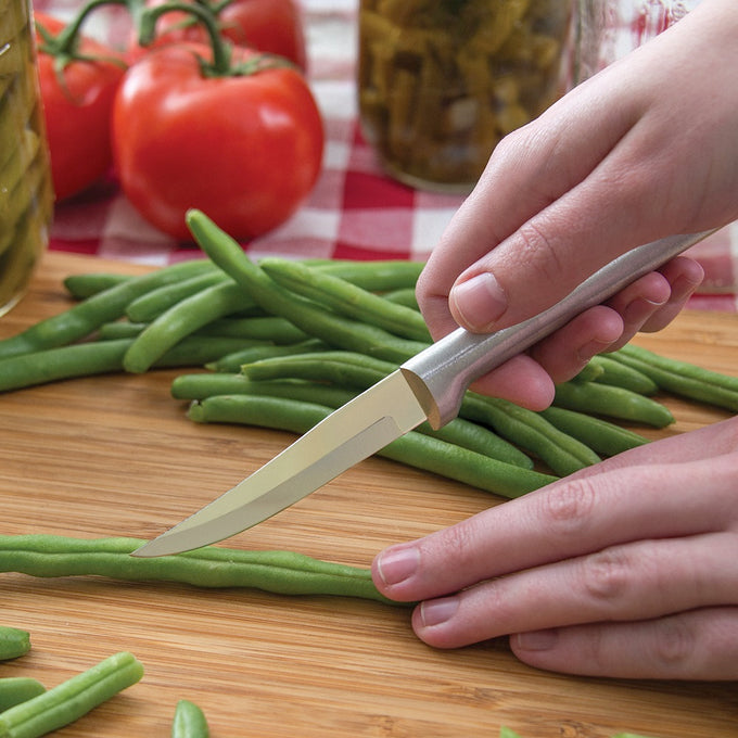 Sharp carbon stainless steel paring knife with cast aluminum handle featuring a non-slip satin finish, slicing fresh green beans on a wooden board in kitchen food prep setting.
