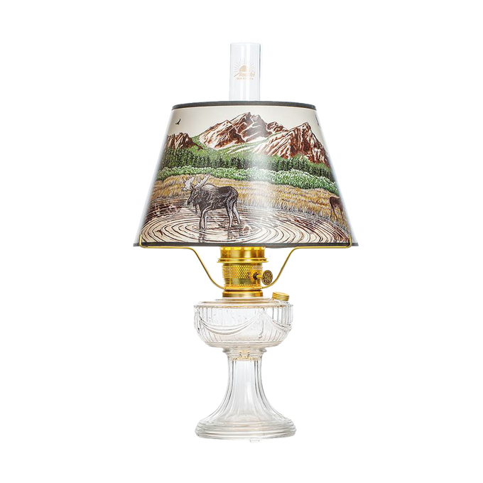 Clear oil lamp with brass burner and a Rocky Mountain scenic parchment shade depicting a moose by a lake with mountains in the background, featured in Lamps & Lighting, Oil Lamps, Table Lamps, Best Sellers, and Promo Eligible collections.