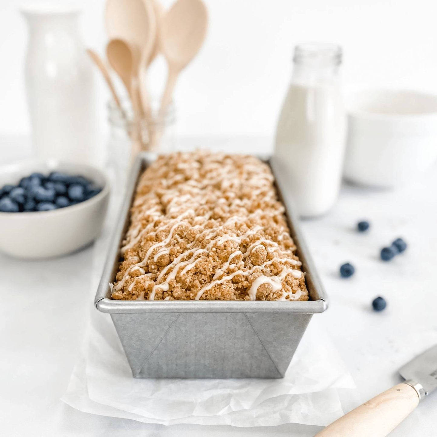Handcrafted nonstick aluminized steel loaf pan made in the USA, filled with crumb-topped bread, styled with blueberries, milk, and wooden utensils, featured in Kitchen & Food and Baking Supplies collections.