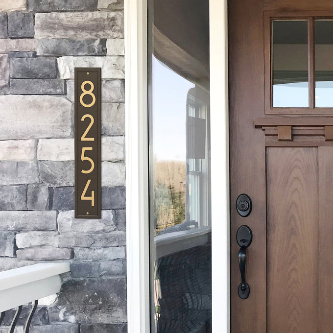 Handcrafted vertical aged bronze address plaque with contemporary numbers mounted on stone siding, enhancing curb appeal, made in USA, featured in Home & Decor and Mailboxes and Address Signs collections.