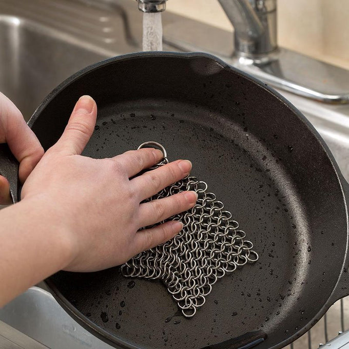 Hand using a stainless steel chainmail cleaner with keyring handle to scrub a cast iron skillet under running water, featured in Home & Decor, Household Cleaning, Cleaning Utensils and Gadgets, Best Sellers, and Promo Eligible collections.