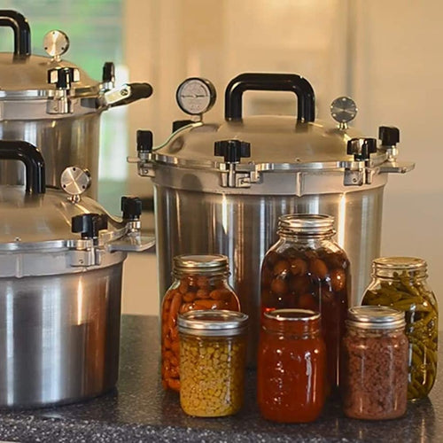 Set of heavy-duty aluminum pressure canners with secure locking lid and pressure gauge, displayed alongside various jars of preserved vegetables and sauces, ideal for food preservation collections.