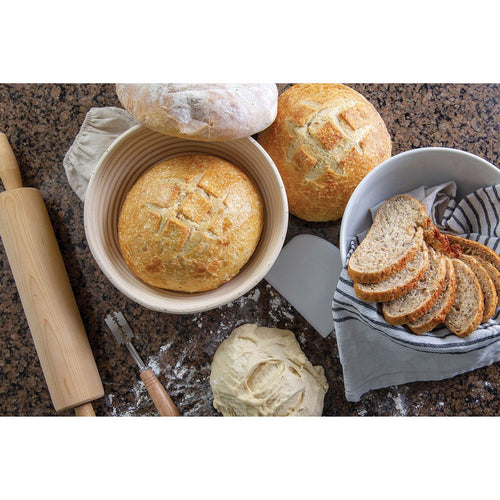 Handcrafted rattan bread proofing basket with removable liner holding a round loaf, surrounded by dough, sliced bread in a cloth-lined bowl, and baking tools, perfect for Kitchen & Food and Baking Supplies collections.