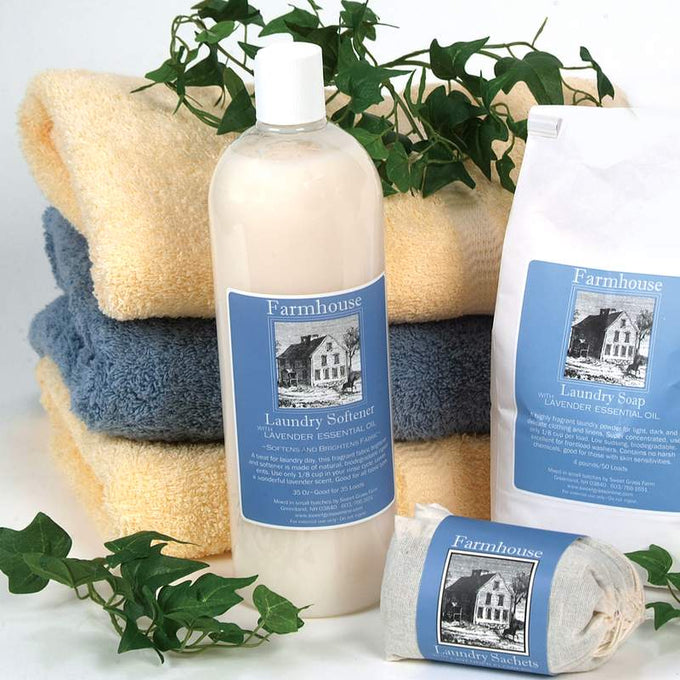 Clear bottle of handcrafted fabric softener with lavender essential oil label, surrounded by soft folded towels, laundry soap, and sachets with green leaves, fitting Home & Decor, Laundry Supplies, USA Made, Best Sellers, and Promo Eligible collections.
