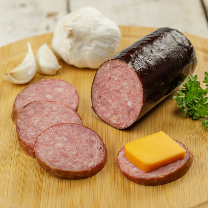 Handcrafted summer sausage from Amish Country made in USA, sliced on a wooden board with fresh garlic, parsley, and cheese, ideal for Kitchen & Food, Snacks and Sweets, and Pantry collections.