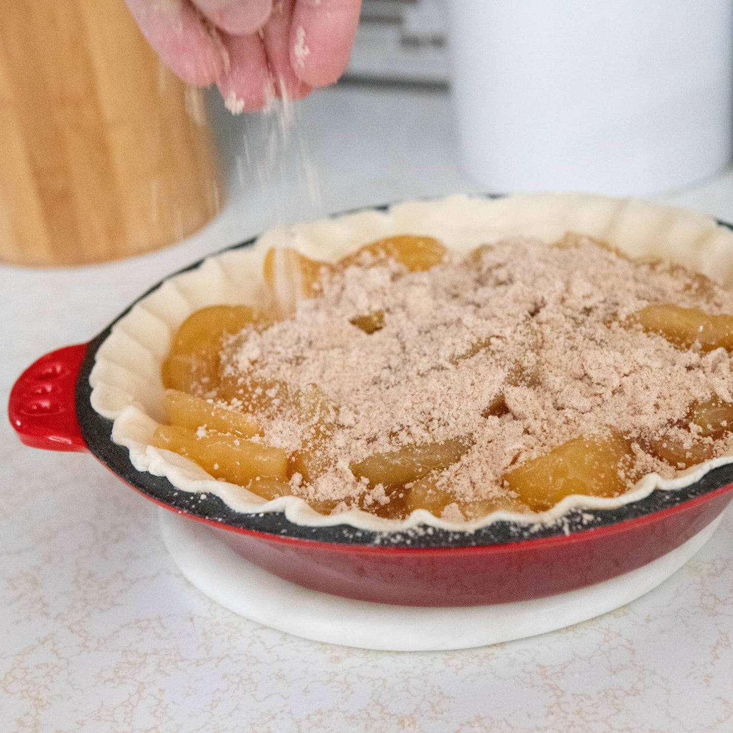 Handcrafted cast iron pie pan with crimped edges and red exterior, filled with sliced fruit and cinnamon sugar being sprinkled, perfect for Kitchen & Food, Cast Iron, Cookware, Baking Supplies, Best Sellers, and Promo Eligible collections.